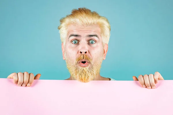 Surprised blonde bearded man holding empty paper. Discount sale or season sales. Business man holding a blank banner and looking down to copy space.