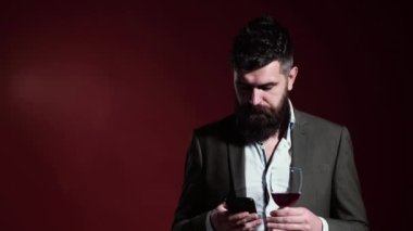 Sommelier şarabın tadını alır. Alkol içeceği. Telefonlu bir adam. Yakışıklı sakallı erkek pahalı kırmızı şarap içiyor..