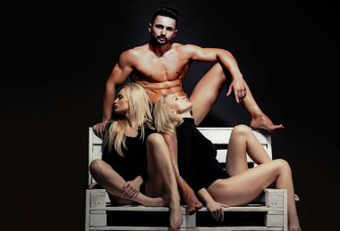 Üçlü aşıklar. Kaslı, ıslak vücutlu ve güçlü atletik gövdeli bir adam. İç çamaşırlı, siyah, lezbiyen ve eşcinsel vücutlu seksi sarışın ikiz kızlar..