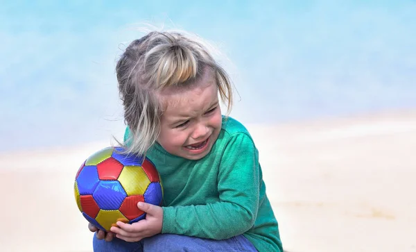 Dziecko płacze siedząc z kolorowym piłką na plaży — Zdjęcie stockowe