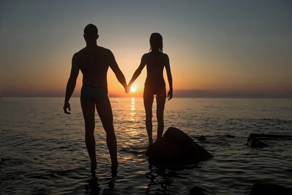 日没とビーチで官能的なカップルのシルエット。ロマンチックなデートを愛するカップルは、海岸で夜に手をつないでいます。ロマンスと愛の概念. — ストック写真