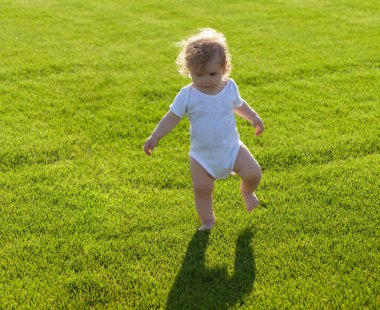 İlk adım. Bebek çıplak bacakları yeşil çimlerin üzerinde duruyor..