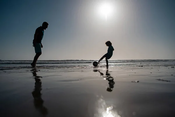 父と息子は夏休みにビーチでサッカーやサッカーをする. — ストック写真