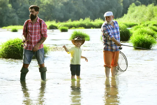 Un hobby maschile. Giornata estiva. Famiglia multigenerazionale maschile. Pescatori familiari che pescano con mulinello. Padre insegnamento figlio come volare-pesce nel fiume. — Foto Stock