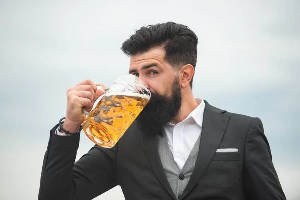 Man in classic suit drinking beer. Bearded guy in classic outfit looks happy and satisfied. Portrait of man with lifted high glass of beer. — Stock Photo, Image