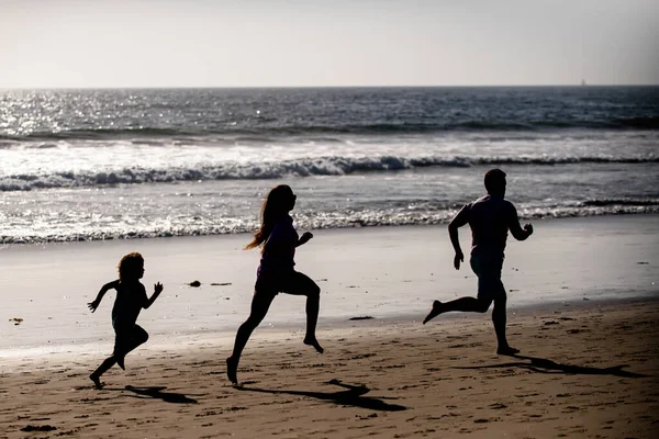 Fitness family running on a sandy beach. Sporty family father, mother and baby son running together. Child with parents run by water along sea. Sport, health on summer. Healthy lifestyle.