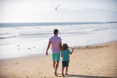 Baba ve oğul yaz plajında yürüyor. Yaşam tarzı ve aile tatili, mutluluk adamı konsepti..