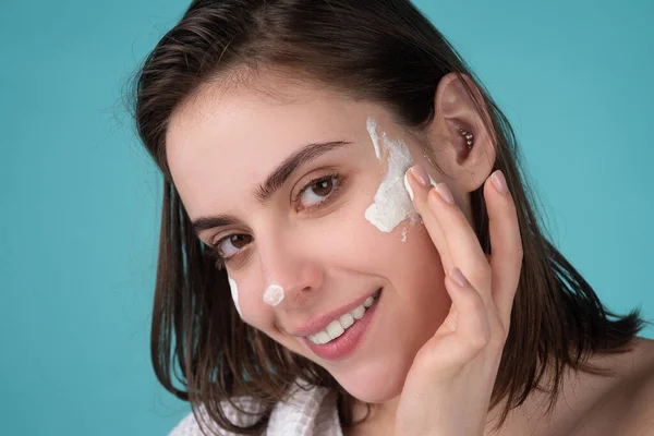 Beautiful young woman with clean fresh skin applying moisturizer cream on her pretty face. — Stock Photo, Image