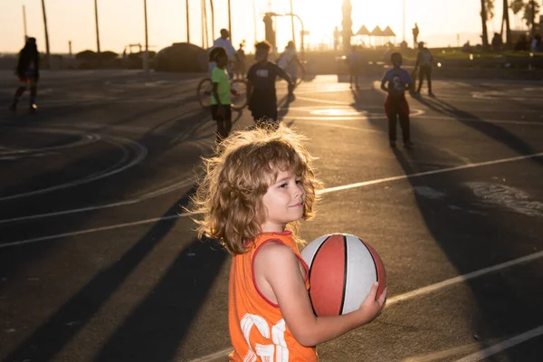 Lindo niño juega baloncesto. Niños activos disfrutando del juego al aire libre con pelota de baloncesto al aire libre al atardecer. —  Fotos de Stock
