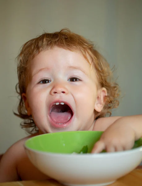 Ritratto di bambino caucasico carino con cucchiaio. Bambino affamato disordinato con piatto dopo aver mangiato purea. — Foto Stock