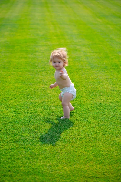 Leuke grappige lachende baby leren kruipen met een luier die plezier heeft met het spelen op het gazon kijken naar de zomer in de tuin. Eerste stap. — Stockfoto