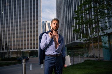 Gömlekli çekici bir adam. Açık havada seksi bir iş adamı. Çekici bir adamın gömleğini çıkarması. Cazibesine güveniyor. Ceketi omuzunda, gömleği açık yakışıklı bir manken..