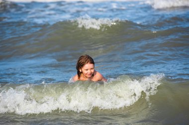 Mutlu çocuk yaz plajında hayatın tadını çıkarıyor. Güneşli bir günde denizde dalgaların arasında küçük bir çocuk. Arka planda okyanus ya da deniz dalgaları.