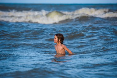 Çocuk yüzüyor, eğleniyor ve denizin dalgalarında zıplıyor. Aile için deniz tatili.