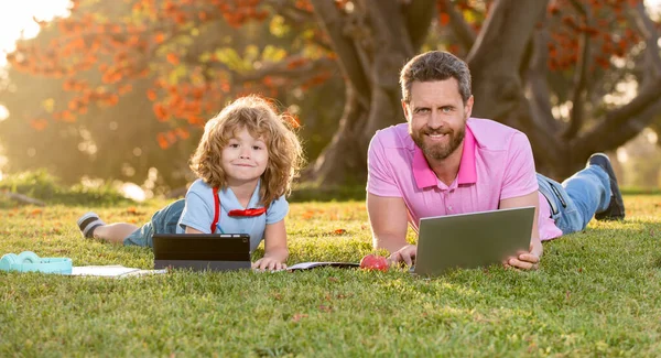 Outdoor learning. Father and son playing or studying with laptop in the park.