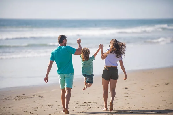 Achteraanzicht van gelukkige jonge familie wandelen op het strand. Kind met ouders die elkaars hand vasthouden. Volledige lengte gedicht. — Stockfoto
