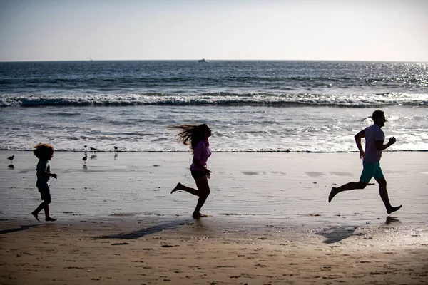海の近くを走るフィットネスファミリーのシルエット。子供と屋外フィットネスのためのスポーツのための家族のジョギング. — ストック写真