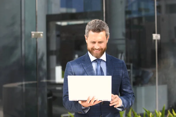 Business man holding laptop standing on the street near business office building.