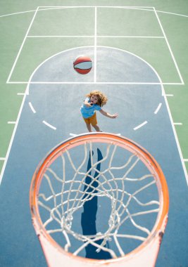 Basketbol formalı çocuk basket sahasında basket topuyla zıplıyor..