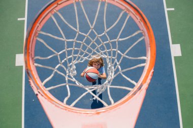 Çocuk bahçesinde basketbol oynayan çocuğun üzerinden açılı görüş.