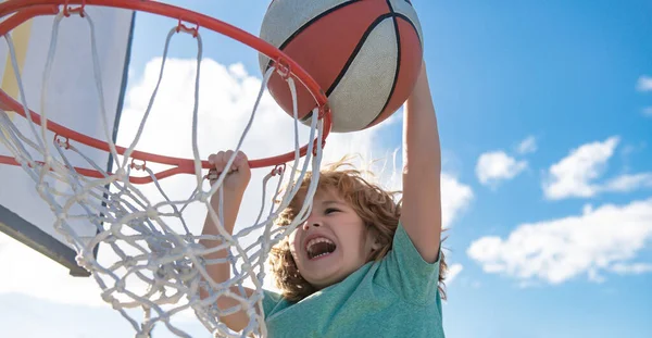 Close-up beeld van kid basketballer maken slam dunk tijdens basketbal spel in schijnwerpers basketbalveld. De kindspeler draagt sportkleding. — Stockfoto