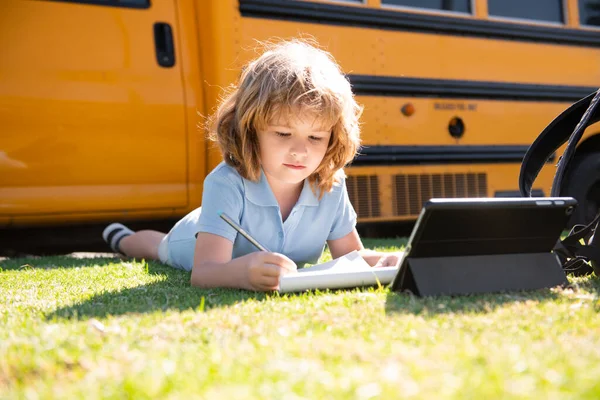 Porträt eines kleinen Schülers, der draußen im Schulhofpark schreibt und Hausaufgaben macht. — Stockfoto