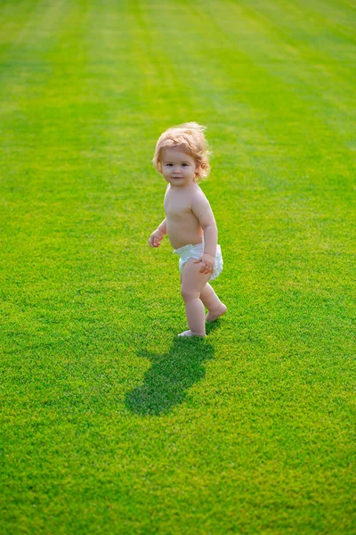 Bebé feliz en la hierba en el fieald en la noche de verano. Niño sonriente usando un pañal al aire libre. Feliz infancia y cuidado de niños. — Foto de Stock