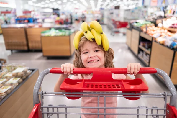 Bambino con carrello della spesa in drogheria o supermercato. Ragazzo che compra frutta di banana nel mercato alimentare. — Foto Stock