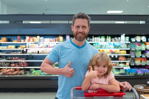 Padre e hijo compran verduras frescas en la tienda de comestibles con los pulgares arriba. Familia en tienda. —  Fotos de Stock