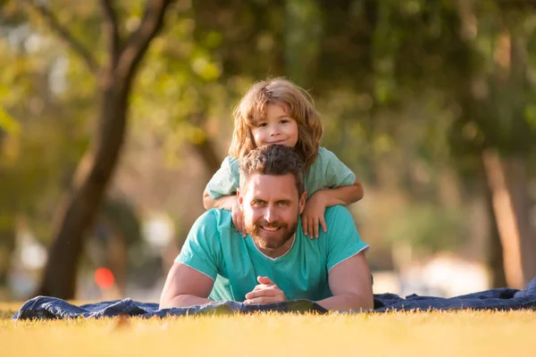 Baba ve oğul çimlerin üzerinde yatıyor. İnsanlar dışarıda eğleniyor. Mutlu tatiller ve dost canlısı aile kavramı.