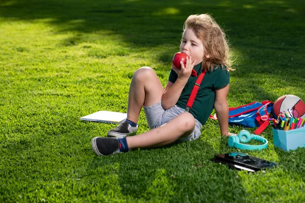 Kid outdoor education. Child doing homework outdoor and eating apple.