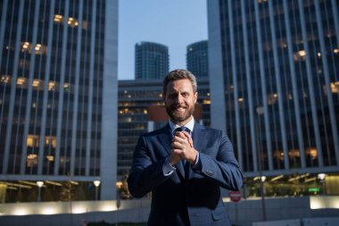 Ofis yakınında takım elbiseli mutlu bir işadamı, başarılı bir işveren geceleri gökdelen bürosunun yanında dururken anlaşma yapıyor..