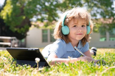 Çocuk mesafesi öğrenme konsepti. Uzaktan eğitim, okul parkında online ders alan bir çocuk. Kalemle kitap yazan bir öğrenci, açık havada çalışmaz. Kendi kendine öğrenim öğrenme. Erken gelişim