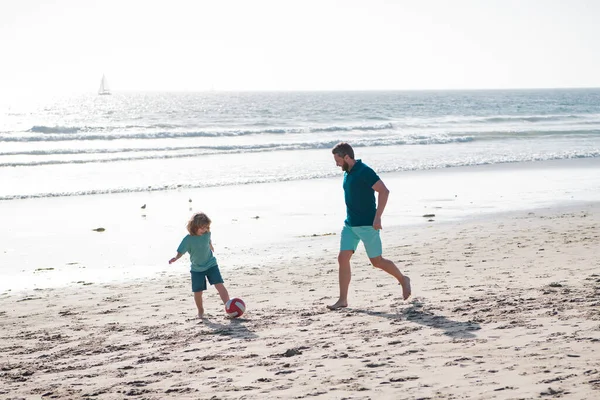 父と子供は屋外で楽しんでいます。父と息子は夏休みにビーチでサッカーやサッカーをします。幼少期と育児の概念. — ストック写真