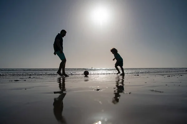 父と息子は夏休みにビーチでサッカーやサッカーをします。夏の日に遊んでいる子供の男の子とパパ. — ストック写真