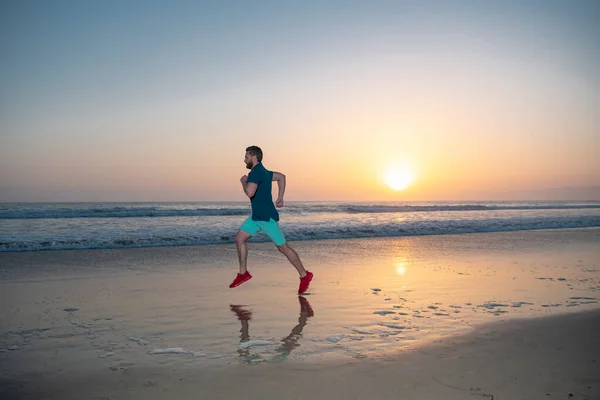 Hombre corriendo en la playa tropical al atardecer. Longitud completa del hombre sano corriendo y corriendo al aire libre. Corredor masculino. Deporte y estilo de vida saludable. —  Fotos de Stock