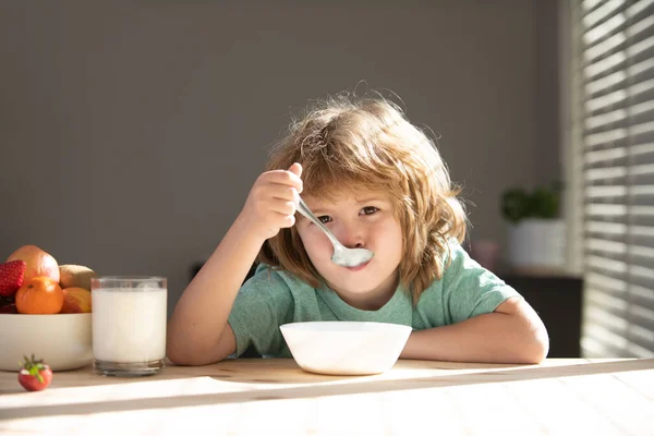 Retrato de un niño comiendo sopa o desayunando. Niño con una cuchara y un plato en la cocina en casa. — Foto de Stock