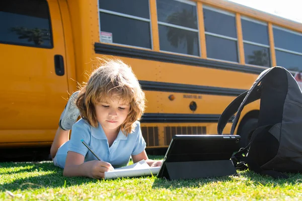Schlauer Schüler auf dem Rasen mit digitalem Tablet im Schulpark. Kind benutzt Geräte, um im Freien zu lernen. Bildung und Lernen für Kinder. — Stockfoto