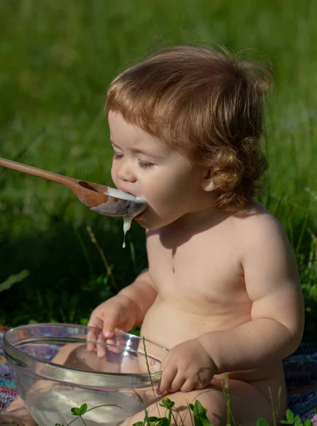 スプーンで赤ちゃんに餌をやります。赤ちゃんの食べ物を緑の芝生の上の屋外で赤ちゃんに与える. — ストック写真