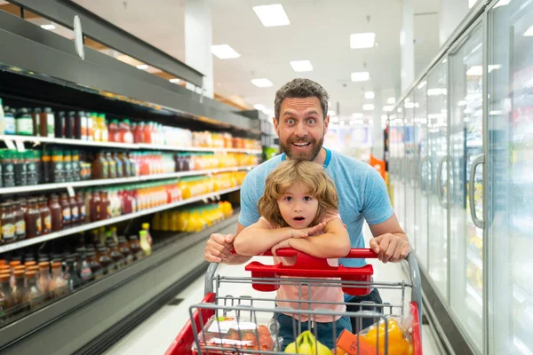 Buon padre sorridente e figlio bambino con carrello della spesa che compra cibo al supermercato o al supermercato. — Foto Stock