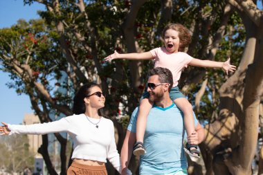 Mutlu aile tatilleri. Neşeli baba, oğlunu sırtında taşıyor. Mutlu ebeveynler oğluyla el ele tutuşur ve güneşli yaz Citi sokağında yürürler, hassas aile anları..