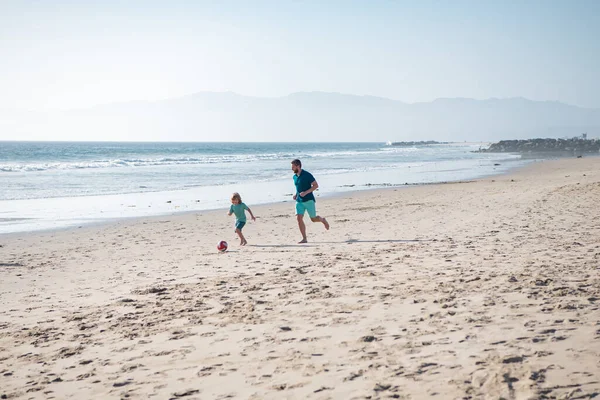 父と息子は夏休みにビーチでサッカーやサッカーをします。屋外で楽しむお父さんと子供。週末の男の家族の概念. — ストック写真