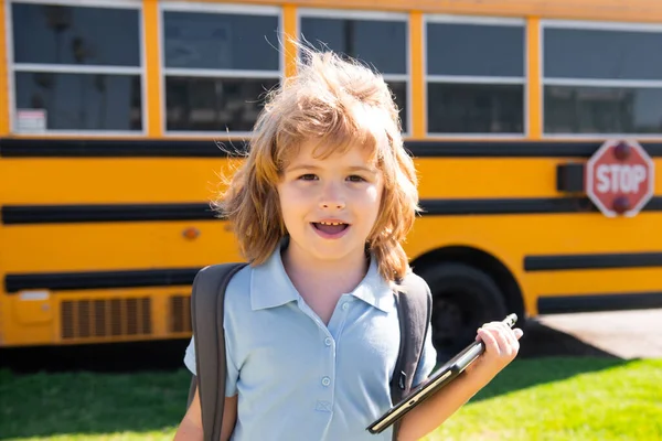 Intelligenter Schüler mit digitalem Tablet im Schulpark in der Nähe des Schulbusses. Bildung und Lernen für Kinder. — Stockfoto