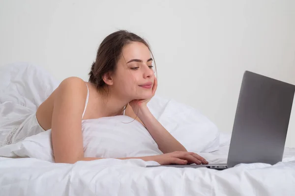 Il concetto di casa di lavoro. Bella donna sdraiata sul letto blogging sul computer portatile in camera da letto. — Foto Stock