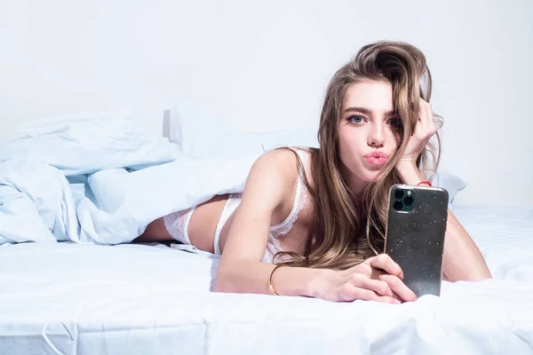 Sexy hermosa mujer con un teléfono inteligente en la cama. Hermosa chica sensual haciendo selfie con su teléfono celular en su dormitorio. —  Fotos de Stock