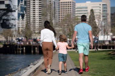 Mutlu Amerikan ebeveynlerinin oğluyla el ele tutuşup güneşli yaz Citi sokağında yürümelerini..