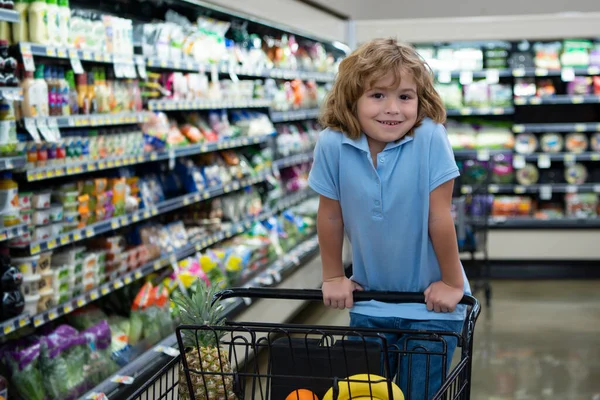 Милый ребенок в продуктовом или супермаркете с товарами в тележке. — стоковое фото