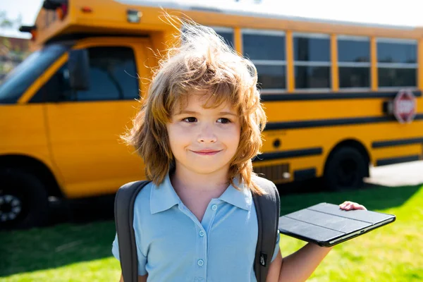Ученик с планшетом возле школьного автобуса. Социальная дистанция во время карантина, концепция он-лайн образования, домашнее обучение снаружи. — стоковое фото