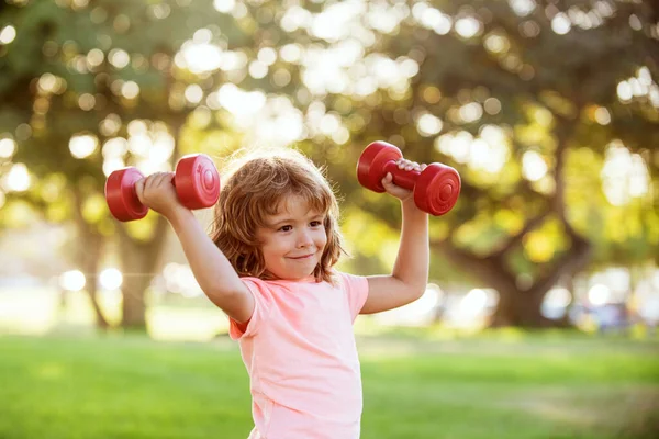 Treino de rapazes no parque. Miúdo. Criança se exercitando com halteres. Criança desportiva com halteres ao ar livre. Desporto infantil. Crianças ativo estilo de vida saudável. — Fotografia de Stock