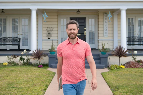 Porträt eines gutaussehenden jungen Mannes, der vor seinem neuen Zuhause spaziert. Erfolgreicher Immobilienmakler kauft Haus für Investitionszwecke. — Stockfoto